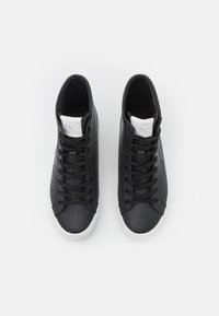 Svarta högsnörade sneakers i slät läder med en vit gummisula. Har svarta snören och en vit tungmärke.