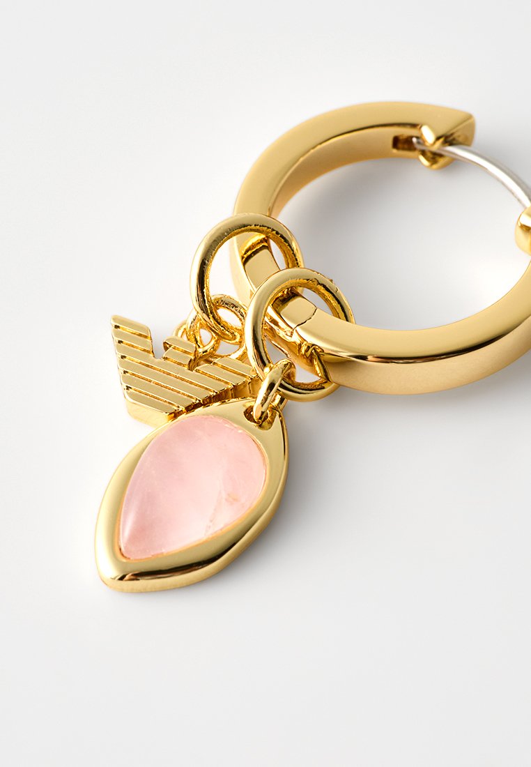 Złoty kolczyk w kształcie koła o gładkim wykończeniu, ozdobiony różowym kamieniem w kształcie kropli i akcentami w formie geometrycznych charms. Szczegóły z trzema splecionymi pierścieniami.