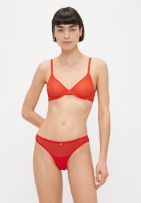 Piros fehérnemű szett, amely sima, párnázott melltartóból áll vékony, állítható pántokkal, valamint hozzáillő, áttetsző tanga kis díszítő részlettel.