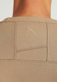 Textil beige con costura texturizada, que presenta un detalle bordado angular en la parte posterior. Diseño simple y ajustado con bordes acanalados.