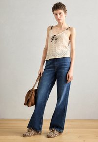 Cami beige con pizzi neri, abbinato a jeans svasati blu scuro e scarpe con stampa leopardata, completato da una borsa a spalla marrone.
