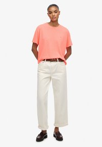 Lyserød bomulds T-shirt med rund hals, parret med opgrebne, off-white bukser med vidde og mørkebrune loafers. Simpelt design.