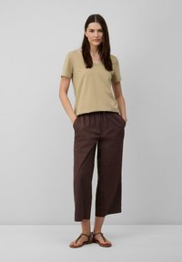 Beige V-Ausschnitt T-Shirt mit kurzen Ärmeln, kombiniert mit braunen Capris. Das Modell trägt braune Sandalen mit einem dekorativen Riemen.