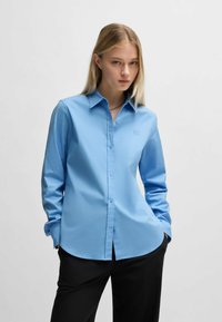 Camicia button-up azzurro chiaro in tessuto morbido con maniche lunghe, dotata di colletto a punta e un sottile logo ricamato sul petto.