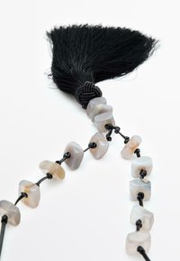 Tassel noir attaché à un collier composé de perles de gemmes grises translucides, enfilées sur un cordon noir, avec des formes géométriques variées.