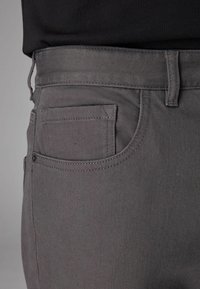 Grå denimbukser med en sidelomme, stikkede detaljer og lige snit. Materialet har en tekstureret overflade. Taljen er blød og fleksibel.