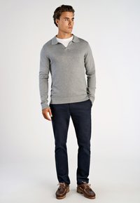 Grå v-ringad tröja med krage, kombinerad med marinblå byxor och bruna segelskor med snörning och gummisula.