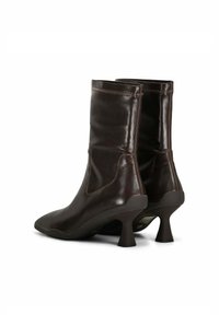 Bottines en cuir marron avec des orteils pointus et des talons courts évasés. Texture lisse avec des coutures visibles le long des coutures.