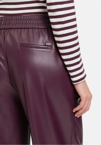Bordeaux faux leather broek met een stijlvolle afwerking, voorzien van een elastische tailleband en een klein zakje op de achterkant. Gestreepte top zichtbaar bij de manchetten.