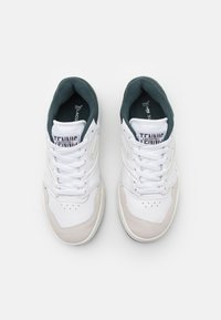 Paire de chaussures de tennis blanches Lacoste avec lacets, doublure intérieure noire et détails en daim sur fond blanc.