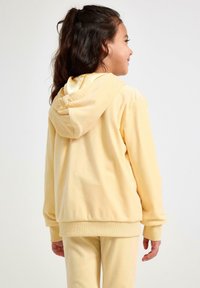 Gul fleece hoodie med snoretræk i hætten og ribbede manchetter, parret med matchende bukser, vist fra bagsiden. Blød tekstur og afslappet pasform.