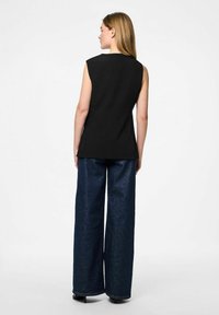 Top noir sans manches au design structuré, associé à un jean en denim bleu foncé à jambe large, présentant une texture lisse et un minimum de détails.