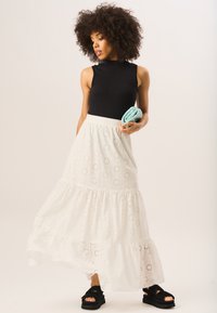 Black ribbed sleeveless top paired with a white eyelet maxi skirt featuring tiered ruffles and floral cutouts. Black sandals complete the look.
