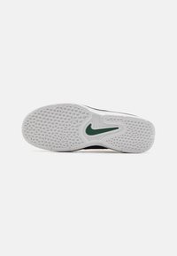 Fekete sportcipő, melynek fehér gumitalpa mintázott és textúrázott, zöld Nike logóval. A talp mintázott tapadást biztosít.