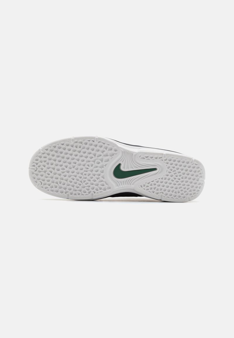 Schwarze Sneaker mit einer strukturierten weißen Gummisohle, die ein grünes Nike-Logo trägt. Die Sohle hat ein gemustertes Profil für besseren Halt.