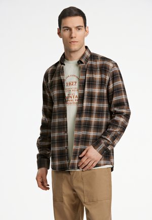 Brown and tan plaid shirt made of woven fabric, buttoned, with a collar. Worn over a light green t-shirt with graphic print.