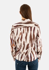 Camicia a maniche lunghe con base beige e strisce astratte marroni e arancioni. Tessuto liscio con colletto standard e polsini con bottone.