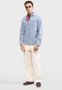 Light blue striped shirt with a button-down design, worn with cream-colored pants and dark brown shoes. Red bandana accents the outfit.