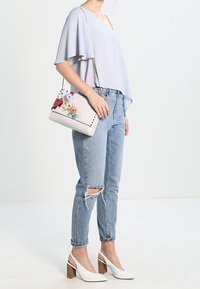 Ljusgrå, flödande topp med spetsiga ärmar, kombinerad med slitna ljusblå jeans. Vita slingback-höga klackar och en flerfärgad blommig väska.