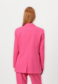 Pink tailored blazer with a single vent at the back and notched lapels. Smooth fabric, structured shoulders, and long sleeves.