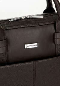 Bolso de mano de cuero marrón con una superficie texturizada, herrajes de plata con el nombre de la marca y dos asas superiores para llevar.