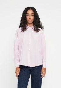 Chemise rose clair à boutons avec col, manches longues et coupe droite. Texture lisse, avec des boutons blancs sur le devant.