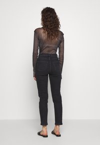 Haut noir transparent à manches longues, avec une coupe ajustée et des paillettes discrètes, associé à un jean taille haute foncé et des sandales noires.