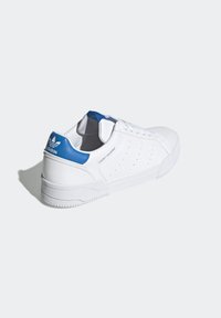 White leather sneaker with a textured rubber sole, featuring a blue heel accent and perforated side detailing. Laced design, minimalist style.