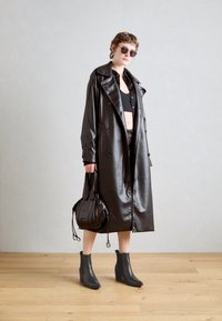Černý kožený trench coat s dvouřadým zapínáním, doplněný černým crop topem, kalhotami s vysokým pasem a černými kotníkovými botami na klínku.