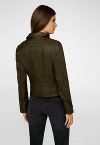 Olivengrønt læderjakke med et tætsiddende design, strukturerede skuldre, subtile syninger og lynlåslommer. Teksturfinish er synlig.