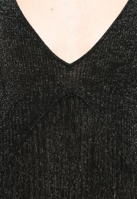 Top em malha canelada preto com fios metálicos, apresentando um decote em V e um detalhe de costura diagonal na área do peito.
