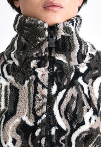 Fleece jacket with high collar, abstract black, white, and brown pattern, full front zipper, textured fabric, and decorative stitching.