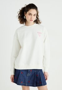 Witte sweatshirt met ronde hals en een roze 'HOWDY'-afbeelding. Gecombineerd met een donkere spijkerrok met rode vlinderborduursels.