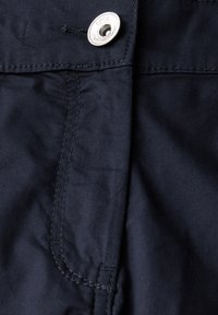 Námořnická modrá bavlněná směsovina s viditelným prošívaným švem, se stříbrným knoflíkem s embosovaným designem a malým detailem boční kapsy.