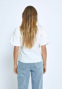 Blusa bianca a maniche a sbuffo con vita aderente, realizzata in tessuto leggero. Abbinata a jeans in denim blu chiaro. Design semplice e pulito.