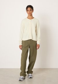 Cream cardigan with button closure, relaxed fit, and ribbed cuffs. Paired with olive green wide-leg pants and gray sneakers.