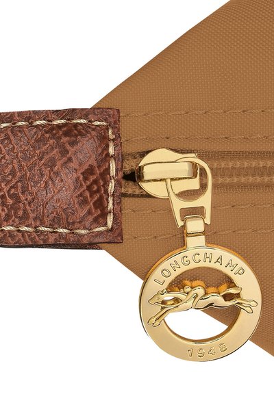 Brown leather trim with a textured finish, gold zipper pull with a circular charm featuring the Longchamp logo and a greyhound design.
