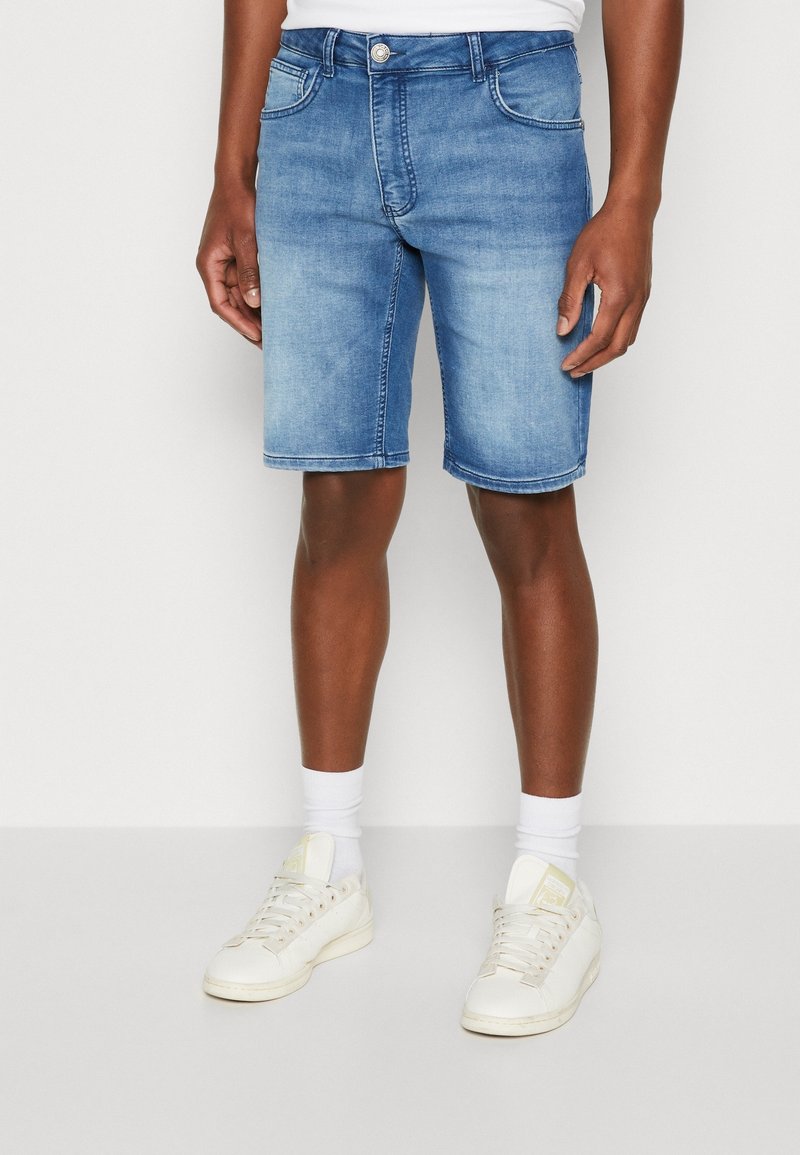 Blue denim shorts with a straight cut, five-pocket design, and subtle fading; paired with white sneakers and crew-length socks.