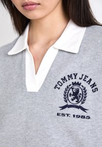 Maglione grigio in cotone con un collo alla francese bianco. Presenta un logo ricamato blu navy e l'anno "EST. 1985" sotto un'immagine di leone.