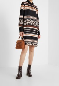 Long-sleeve dress with black, brown, and white stripes, featuring a leopard print panel. Brown purse with rounded handles and embossed detail. Dark ankle boots.
