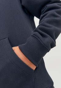 Felpa blu navy con tasca a marsupio e polsini a costine. Il tessuto appare morbido, con una superficie liscia e cuciture minime visibili.