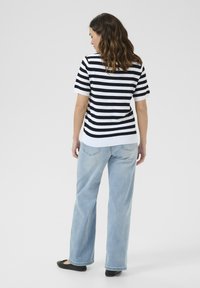 Haut à manches courtes à rayures noires et blanches, coupe décontractée, associé à un jean large bleu clair et des chaussures plates noires. Tissu tricoté texturé.
