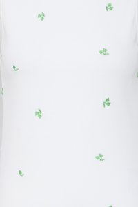 Tissu blanc avec de petits groupes de feuilles vertes brodées dispersés sur la surface.