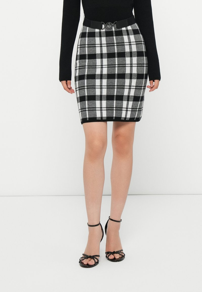 Saia aos quadrados em preto e branco, com design ajustado, tecido texturizado e um cinto preto com fivela circular metálica.