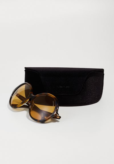 Schildpadbril met bruine lenzen, rond frame en gouden accenten. Zwarte fluwelen hoes met reliëflogo en klepvergrendeling.