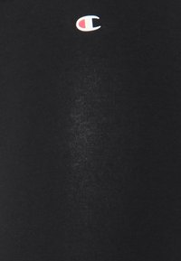 Svart bomullströja med en liten, färgad Champion-logotyp på bröstet. Tyget har en slät textur och minimal glans.