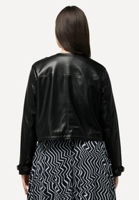 Schwarze Lederjacke im Cropped-Stil mit glatter Textur und langen Ärmeln, kombiniert mit einem rock in Schwarz-Weiß-Zickzack-Muster.