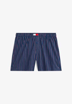 Calzoncillos bóxer azul marino con delgadas rayas verticales rojas y blancas, cintura elástica, botón frontal y parche con el logo de Tommy Hilfiger.