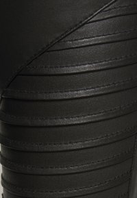 Leggings pretas em imitação de couro com painéis verticais ribeteados, textura suave e costura detalhada ao longo das costuras.