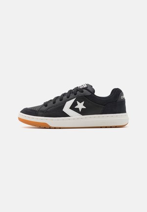 Sort lavtop Converse-sneaker med hvid stjerne-logo, gummisål og sorte snørebånd på hvid baggrund.